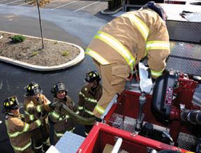 View from top of fire truck of four firemen handing hose from truck