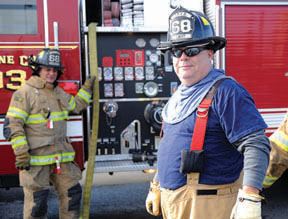 Two smiling uniformed firemen in front of fire truck